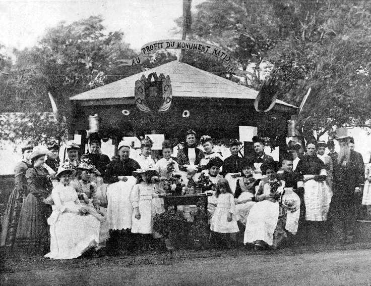 Fotografía antigua en blanco y negro de una tómbola en un parque, con un grupo de personas posando delante